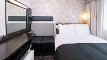 A hotel room with a bed, a desk with a flat-screen TV, a seating area, and a wall-mounted lamp.