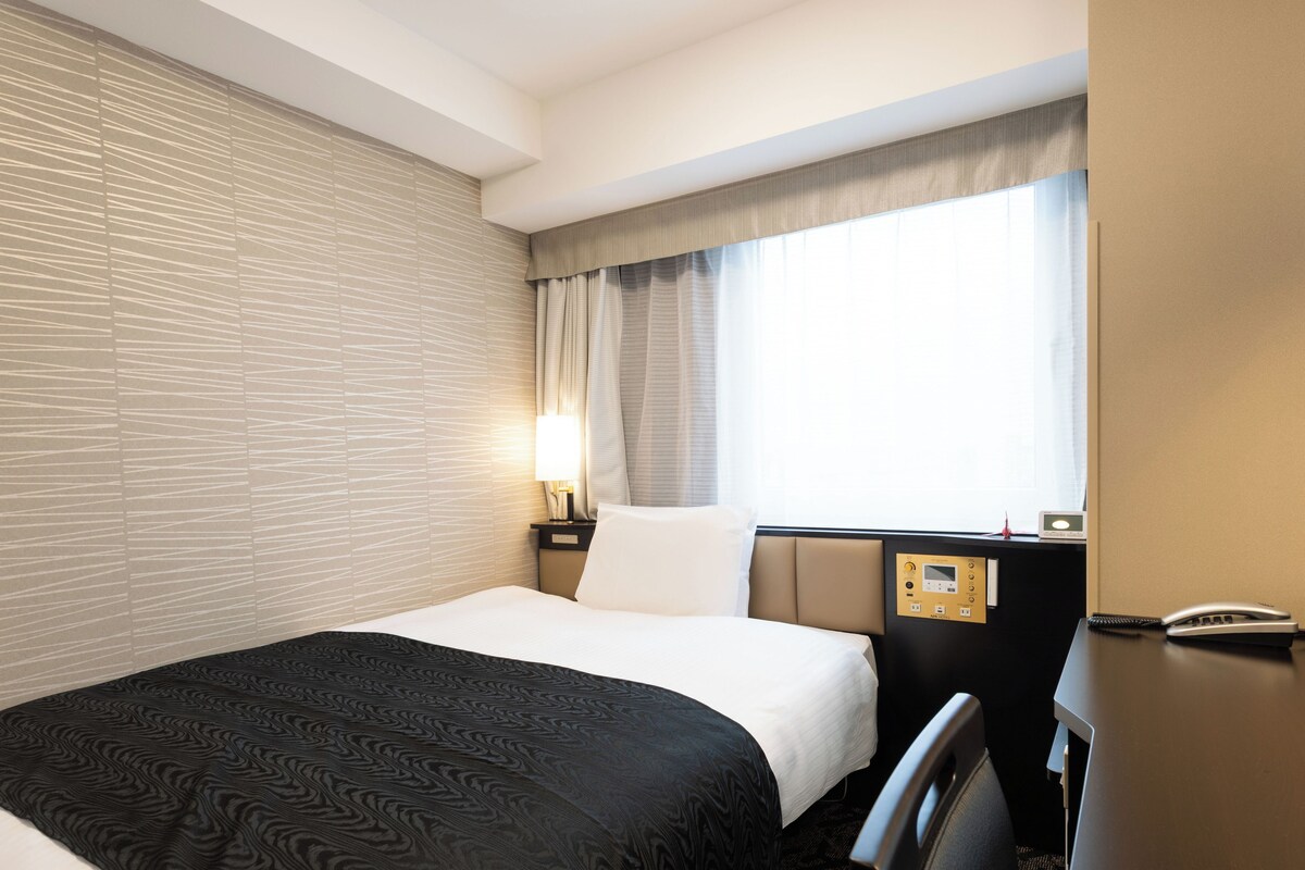 Ein Hotelzimmer mit einem Bett, einem Nachttisch mit Lampe, einer Bedienfeld und einem Telefon.