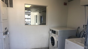 Una sala de bugaderia amb piles de rentadores i assecadores, una finestra petita i un mirall a la paret.