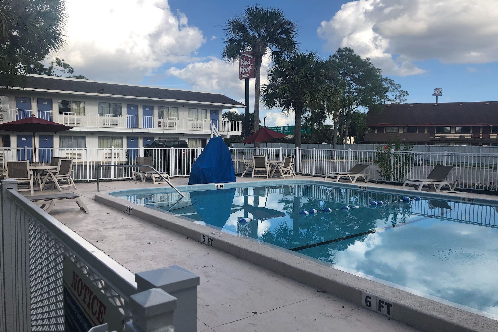 A swimming pool with lounge chairs and umbrellas, surrounded by a fence, with a building in the background.