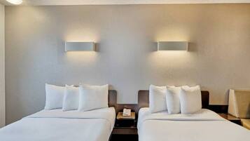 Une chambre d’hôtel avec deux lits, chacun doté de draps et d’oreillers blancs, ainsi que deux tables de chevet avec des lampes.
