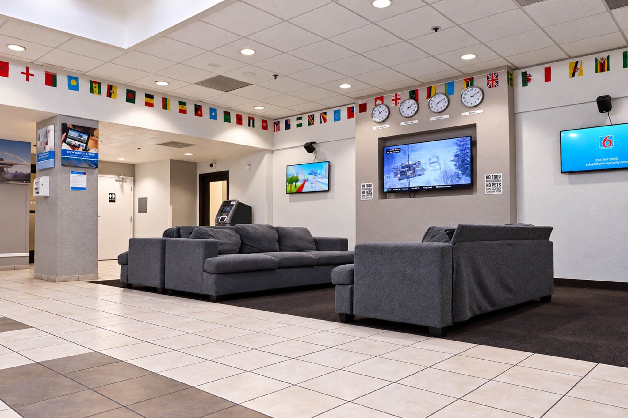 A hotel lobby with grey sofas, a TV screen, and a wall with international flags.