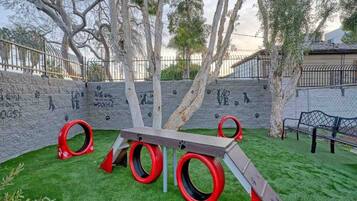 Un parque infantil con tobogán, estructuras para escalar y una zona vallada con grafitis.
