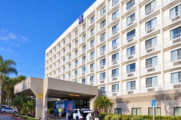 Een meerhoog hotel met een platte gevel, een overdekte ingang en een parkeerplaats met auto's.