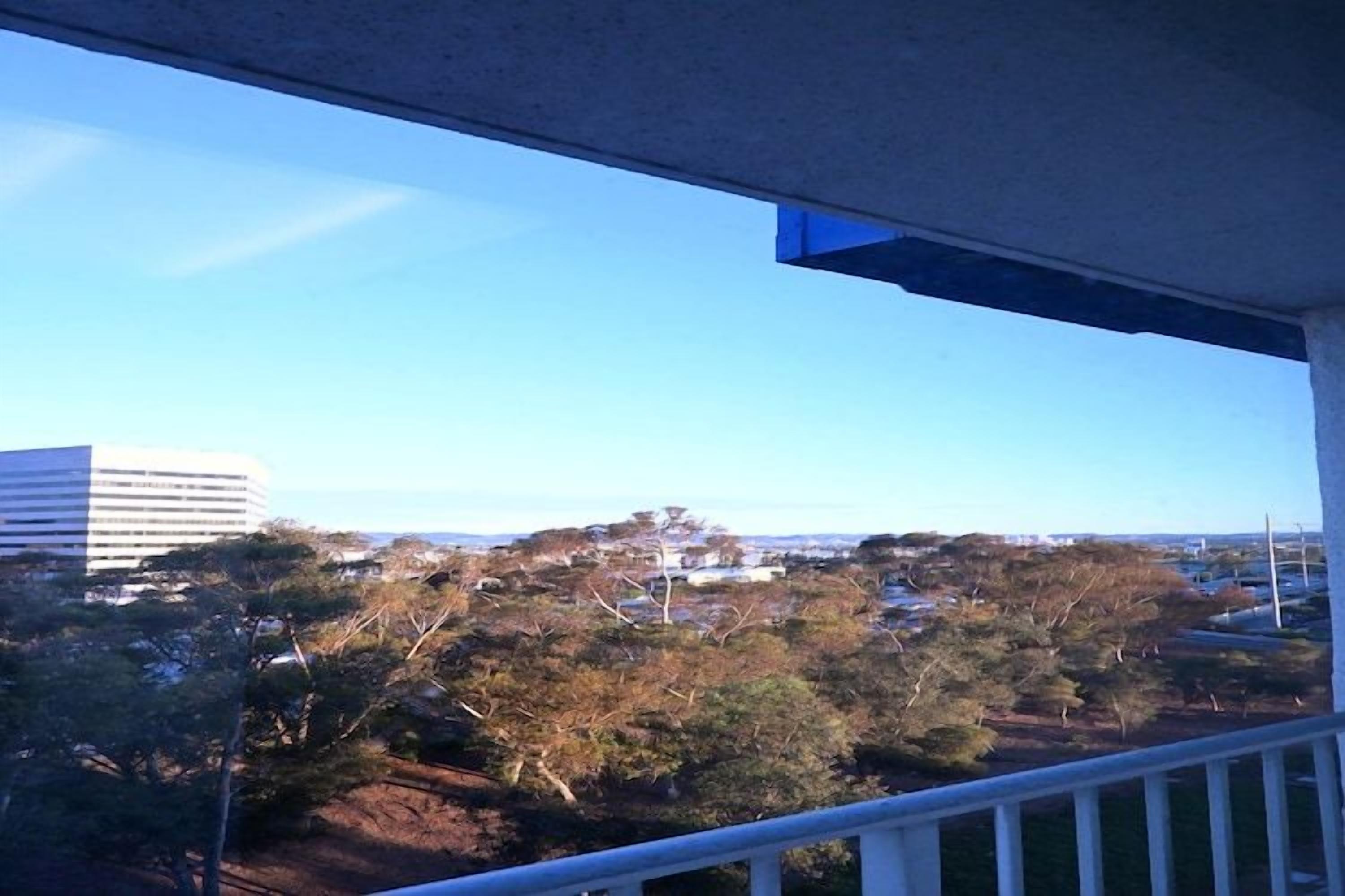 Un balcon donnant sur un paysage urbain, avec notamment un grand immeuble et des arbres.