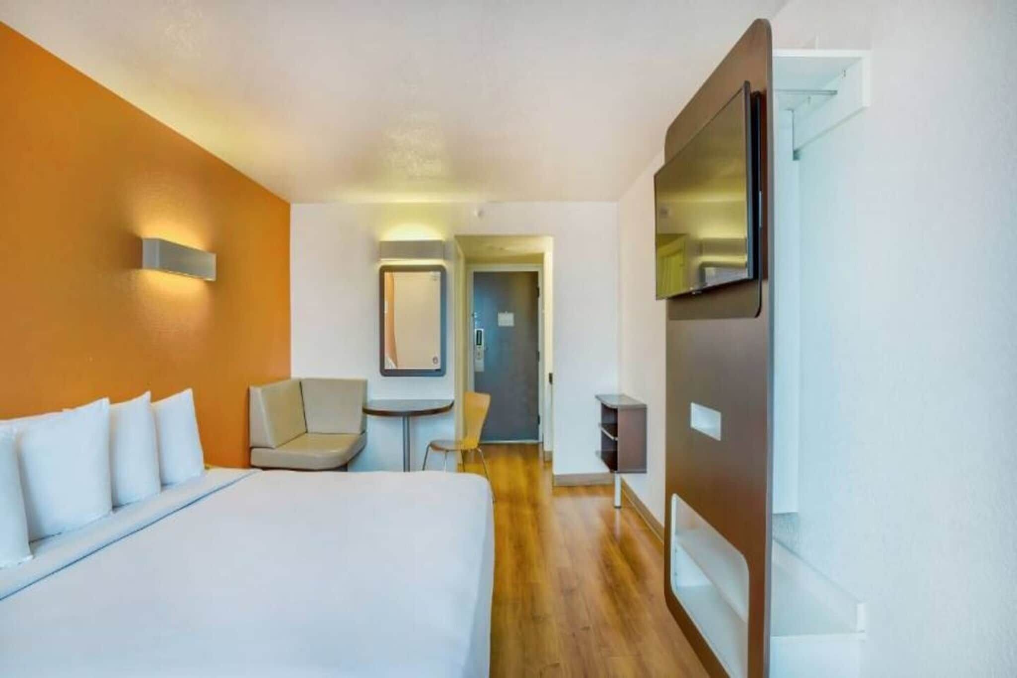 A hotel room with a bed, a chair, a desk, a TV, and a door leading to another room.