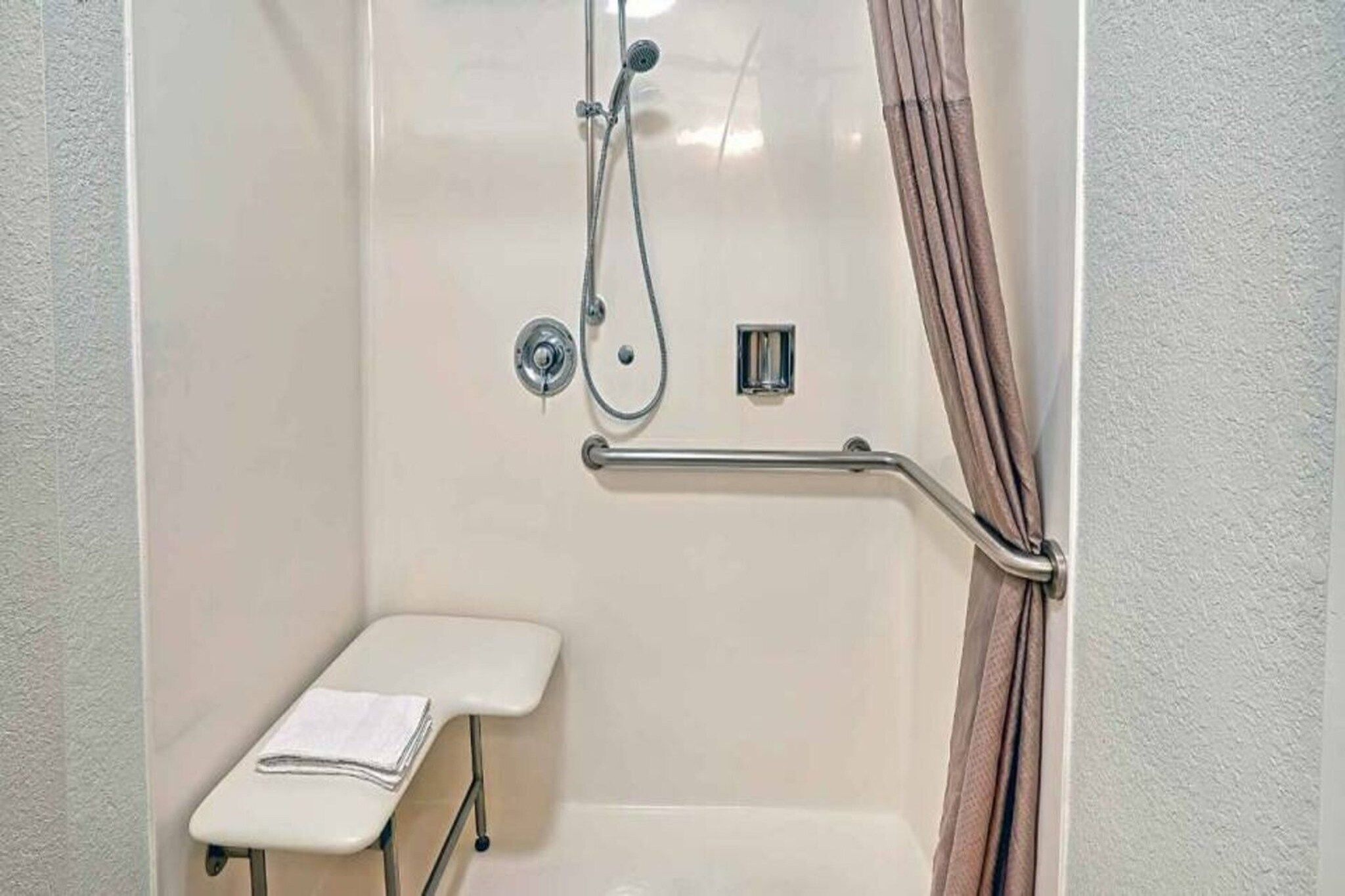 A bathroom with a shower, grab bar, and a small bench.