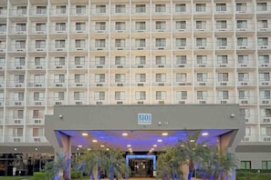 A multi-story hotel with a uniform facade, numbered 5101, featuring a central entrance with a blue-lit canopy and palm trees. - 2 Queen Beds|Premium| Mini Fridge (Inglewood)
