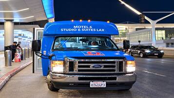 A blue Ford Transit van with 'Motel 6 Suites LAX' written on the front, parked at an airport terminal.