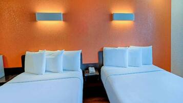 Une chambre d’hôtel avec deux lits simples, une table de chevet et une lampe fixée au mur.