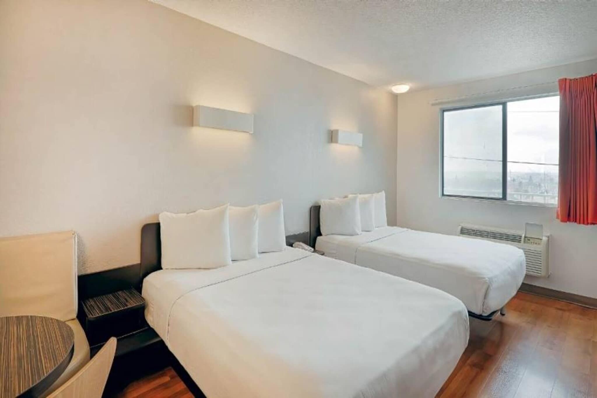 A hotel room with two single beds, a desk, a chair, and a window with curtains.
