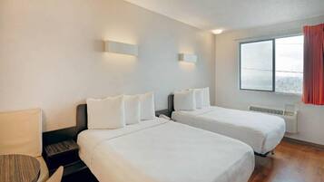 A hotel room with two single beds, a desk, a chair, and a window with curtains.