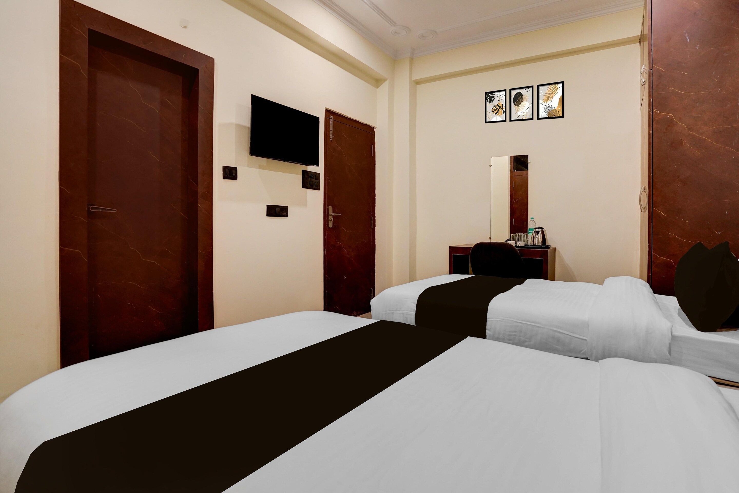 Quarto de hotel com duas camas, televisão, escrivaninha com espelho e obras de arte na parede.