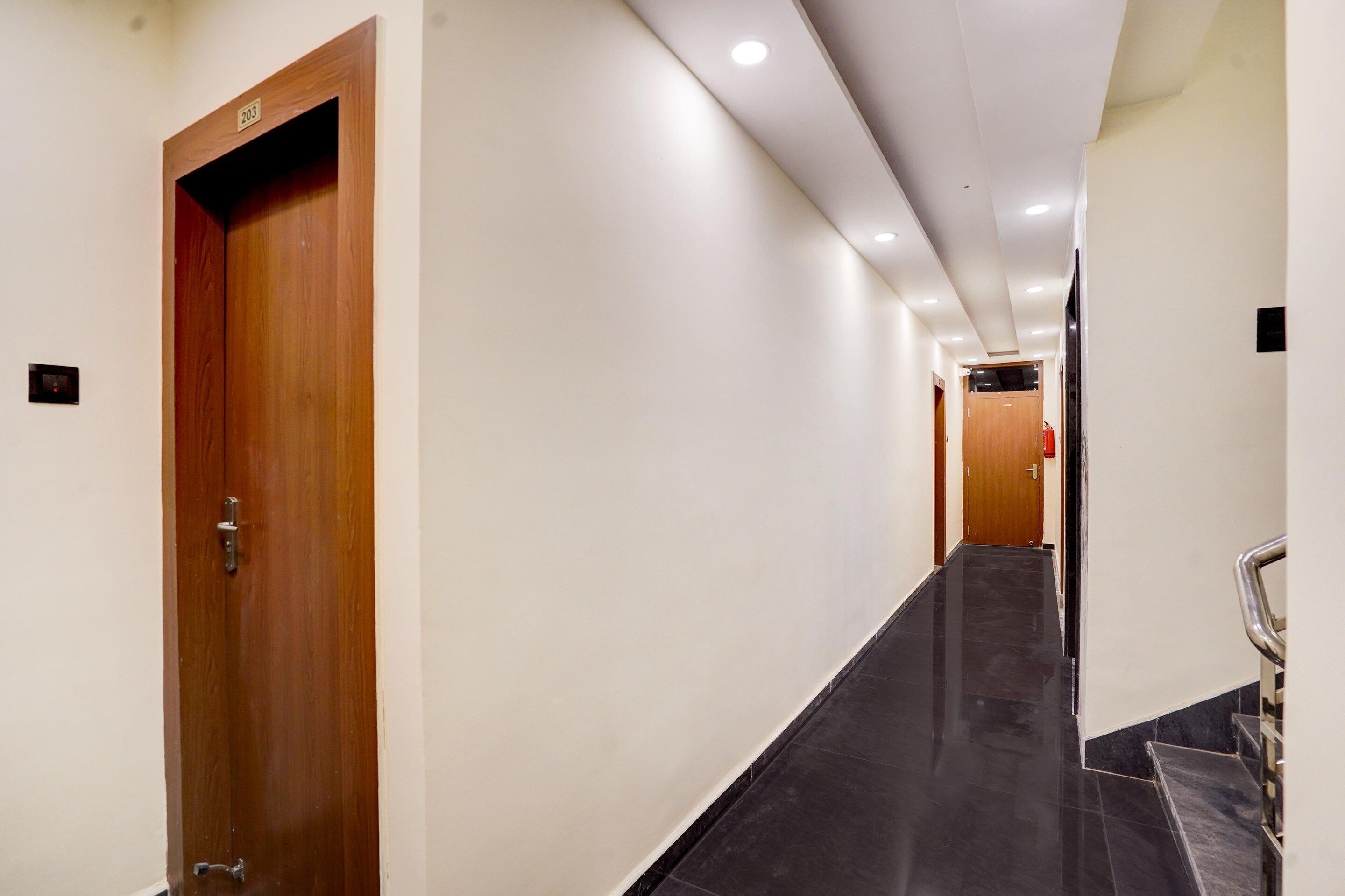 A hallway with a wooden door marked '203', a black tiled floor, and a handrail on the right.