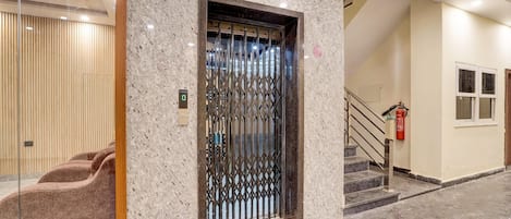 A modern elevator with a metal gate, a staircase with a handrail, and a fire extinguisher mounted on the wall.