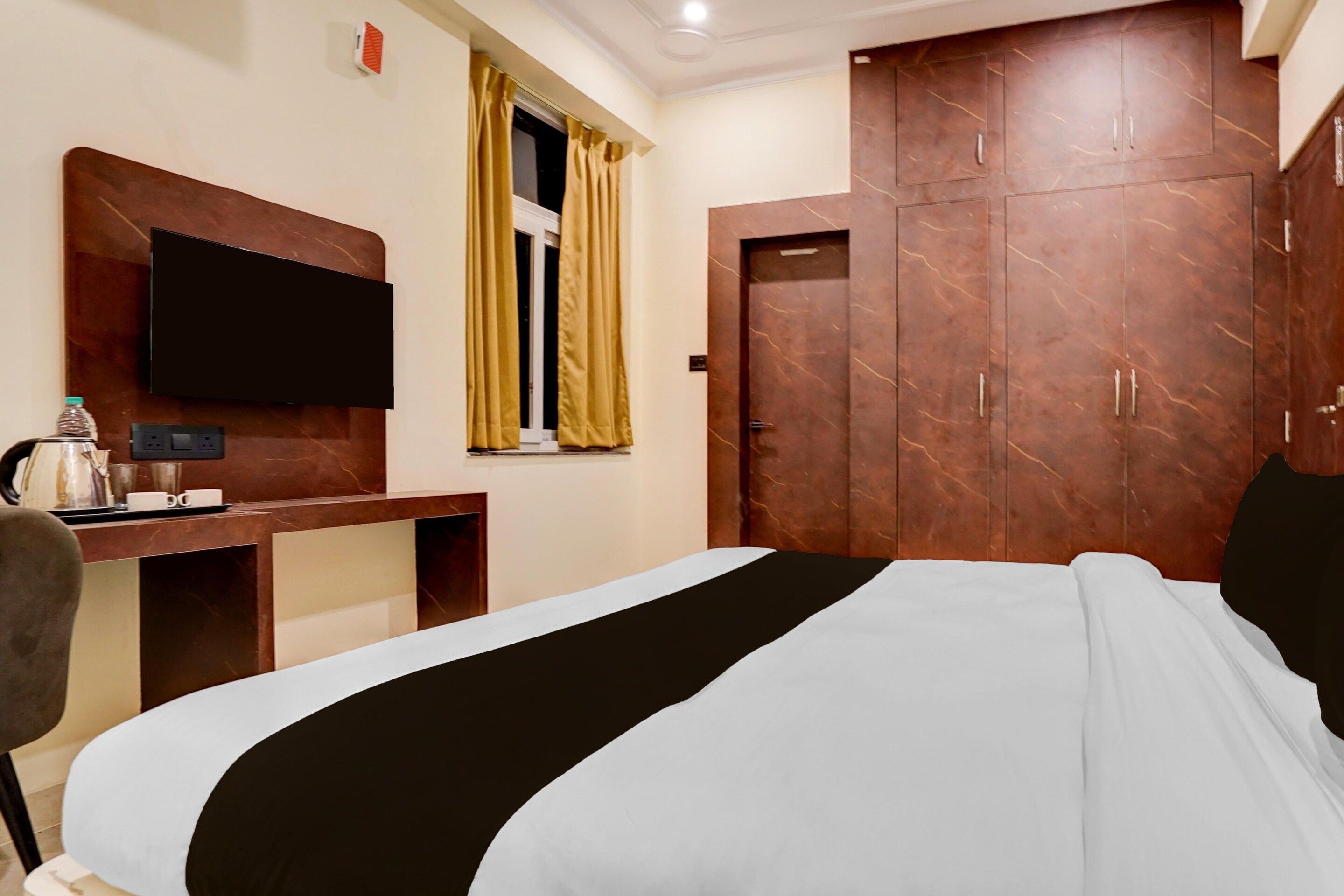 A hotel room with a bed, a desk with a flat-screen TV, a wardrobe, and a window with curtains.
