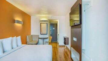 A hotel room with a bed, a chair, a desk, a TV, and a door leading to another room.