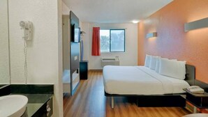 Hotellihuone, jossa on sänky, yöpöytä, peili, ikkuna verhoilla, ilmastointilaite ja seinään kiinnitetty puhelin.