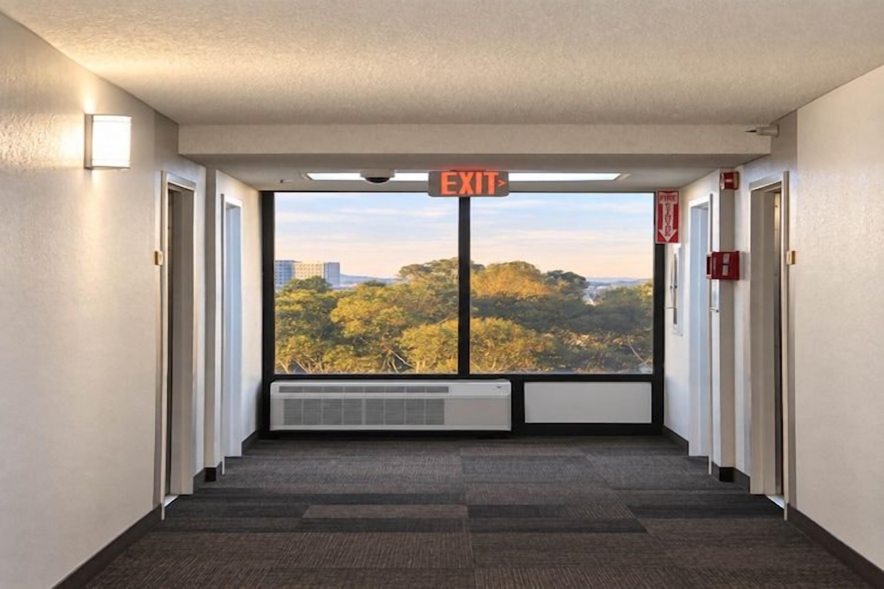 A hallway with an exit sign, a radiator, and a view of trees through a window.