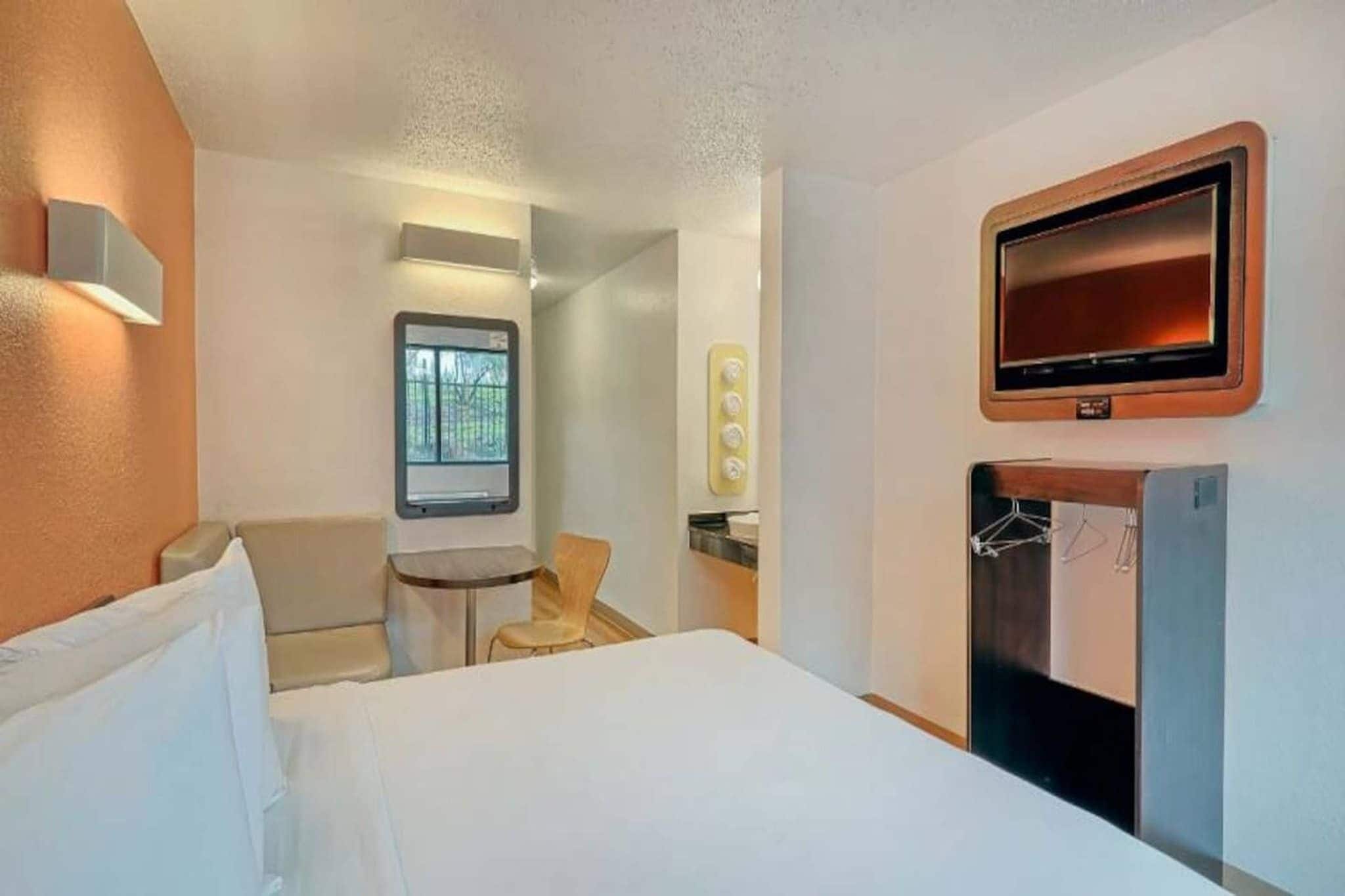 Quarto de hotel com uma cama, uma escrivaninha, uma cadeira, uma televisão e uma janela.