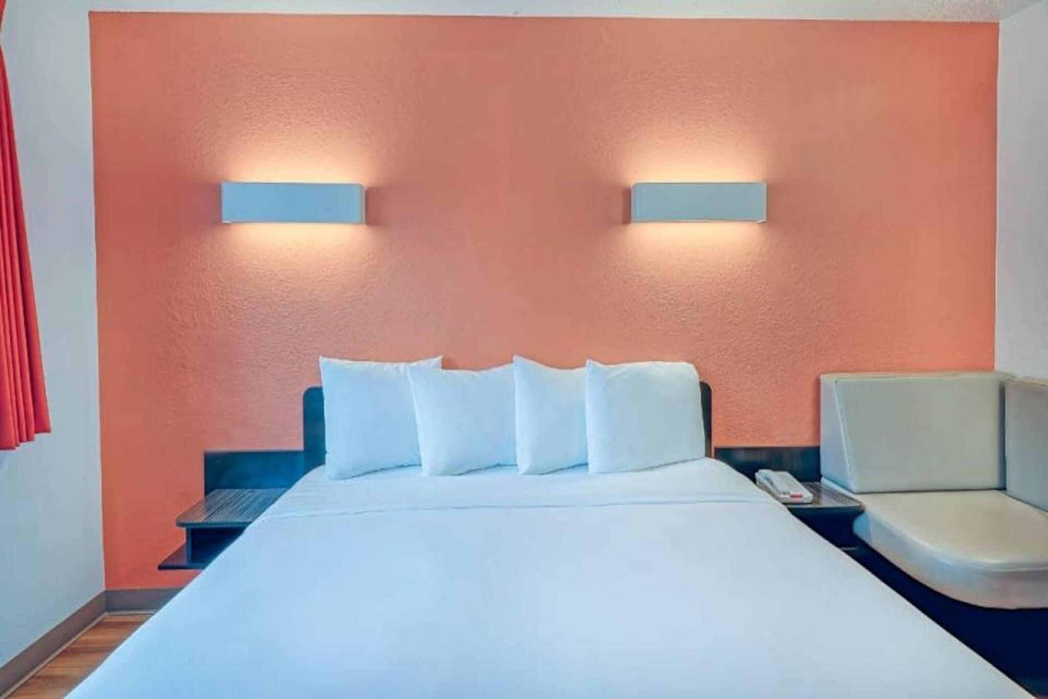 A hotel room with a bed, a nightstand, a chair, and two wall-mounted lights.