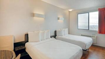Een hotelkamer met twee bedden, een bureau, een stoel en een raam met uitzicht.