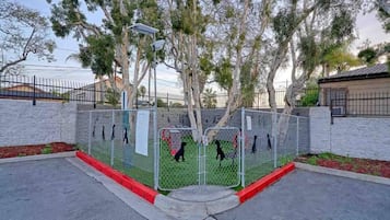 A fenced area with a paved walkway, trees, and a building in the background.