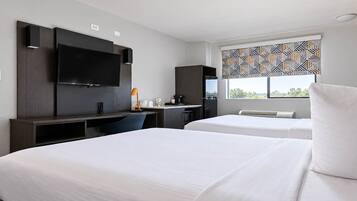 A hotel room with two beds, a desk with a computer, a TV, and a window with a patterned blind.