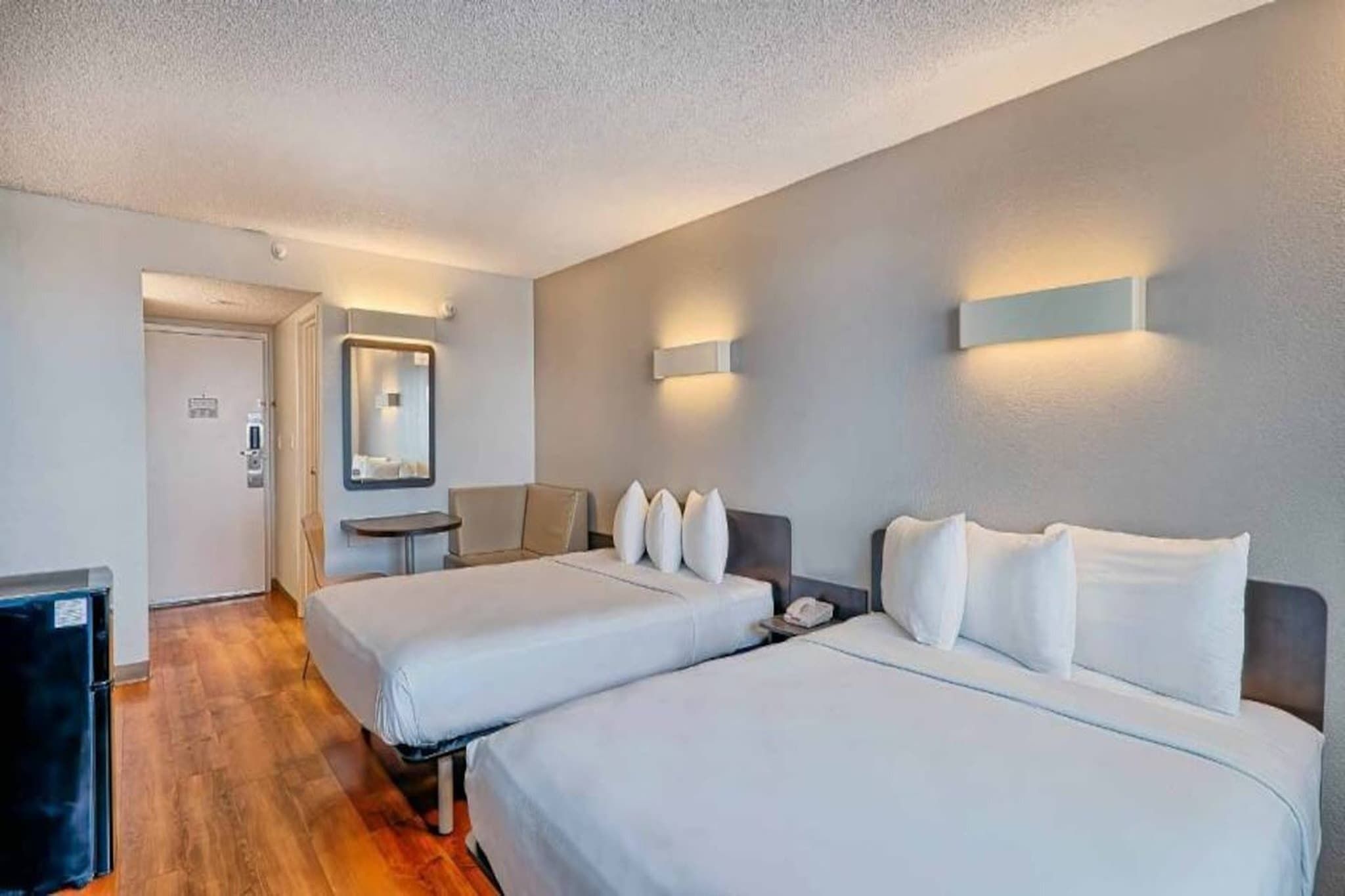 Een hotelkamer met twee bedden, een bureau, een stoel, een spiegel en een prullenbak.