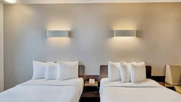 A hotel room with two beds, each with white linens and pillows, and bedside tables with lamps.