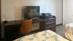 A hotel room with a bed, a desk with a chair, a television, and a dresser.