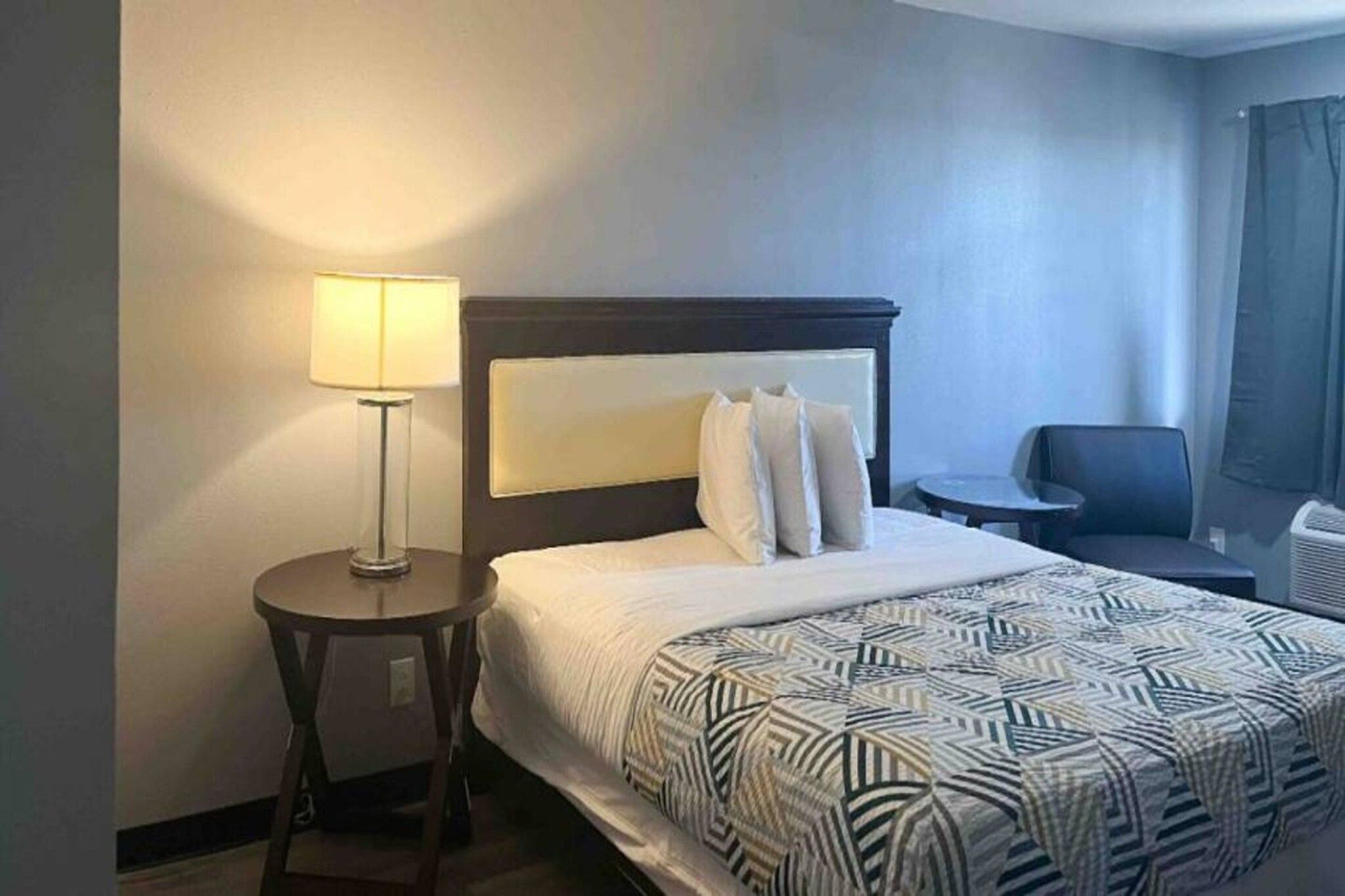 Une chambre d’hôtel avec un lit, une lampe de chevet, une chaise et une petite table.