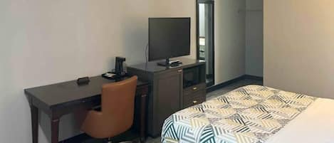 Une chambre d’hôtel comprenant un lit, un bureau avec une chaise, une télévision et un miroir.