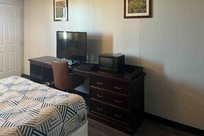 A bedroom with a bed, a desk with a computer, a chair, and a dresser.