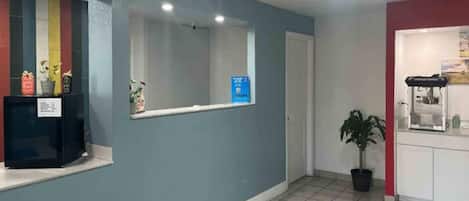 Un espace d’accueil avec un comptoir, une plante en pot et un panneau sur le mur.