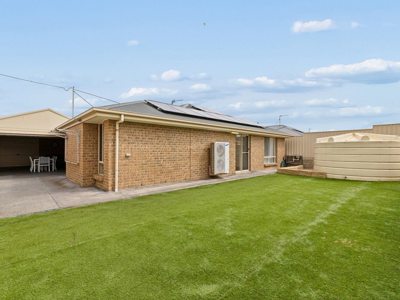 A single-story brick building with a garage, a small patio with a table and chairs, and a well-maintained lawn.