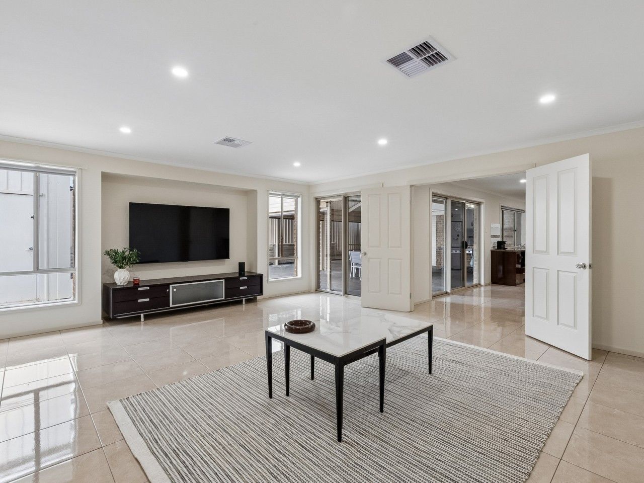 A spacious living room with a flat-screen TV, a dining table, and a large window.