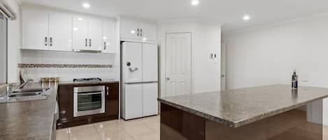 Una cocina moderna con armarios blancos, horno empotrado, refrigerador y una isla grande con encimera de granito.