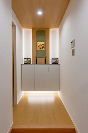 Ein Korridor mit Holzboden, einer grünen Wand mit Kunstwerken, einem weißen Schrank mit zwei Türen und einem kleinen, an der Wand befestigten Gerät.