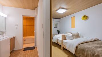 A room with a wooden floor, a bed with white bedding, a bedside table, and a wall-mounted light fixture.
