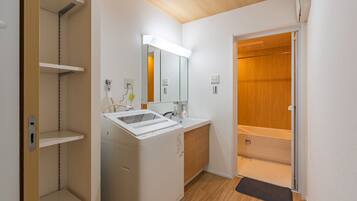 A modern bathroom with a built-in sink, mirror, and a wooden door leading to a shower area.