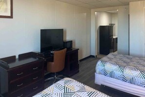 A hotel room with a desk, a television, a microwave, a wardrobe, and two beds with patterned bedding.