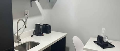 A compact kitchenette with a sink, a toaster, and a small table with a tissue dispenser.
