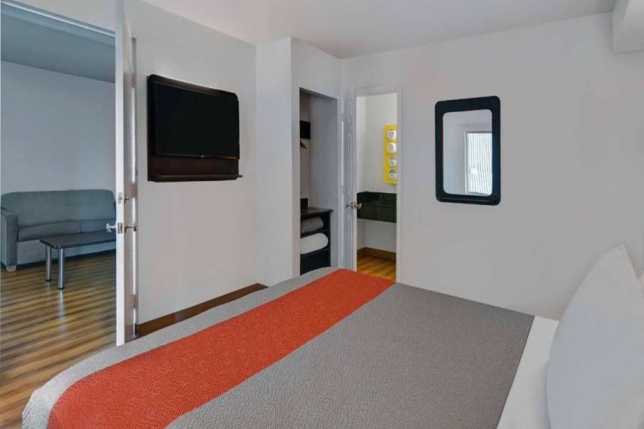 Una habitación de hotel con una cama, un televisor, un espejo y un sofá.
