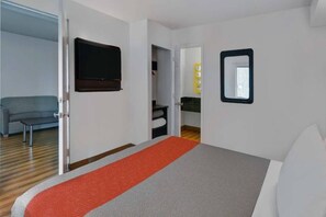 A hotel room with a bed, a TV, a mirror, and a sofa.