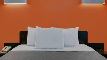 Ein Hotelzimmer mit einem Bett, weißen Kissen, einer grauen Decke, einem Nachttisch mit Telefon und zwei Wandleuchten.