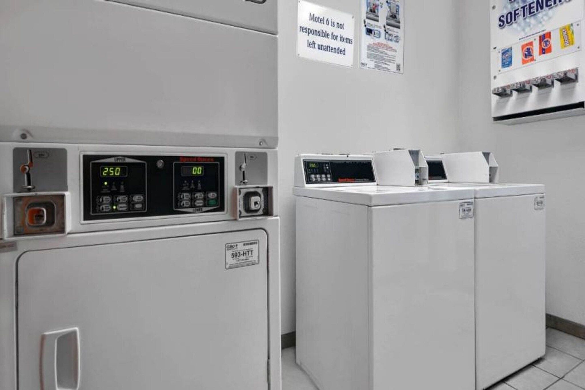 A laundry area with two washing machines, a control panel, and a sign indicating the motel's policy on unattended items.