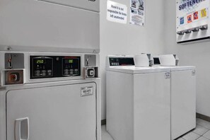 Une buanderie équipée de deux machines à laver, d’un panneau de commande et d’un panneau indiquant les règles du motel concernant les objets laissés sans surveillance.