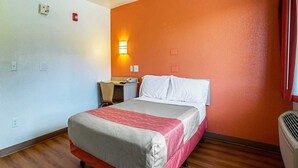 A hotel room with a bed, a desk, a chair, a nightstand, a wall-mounted heater, and a window with curtains. - 1 Queen Bed | Prescott (Prescott)