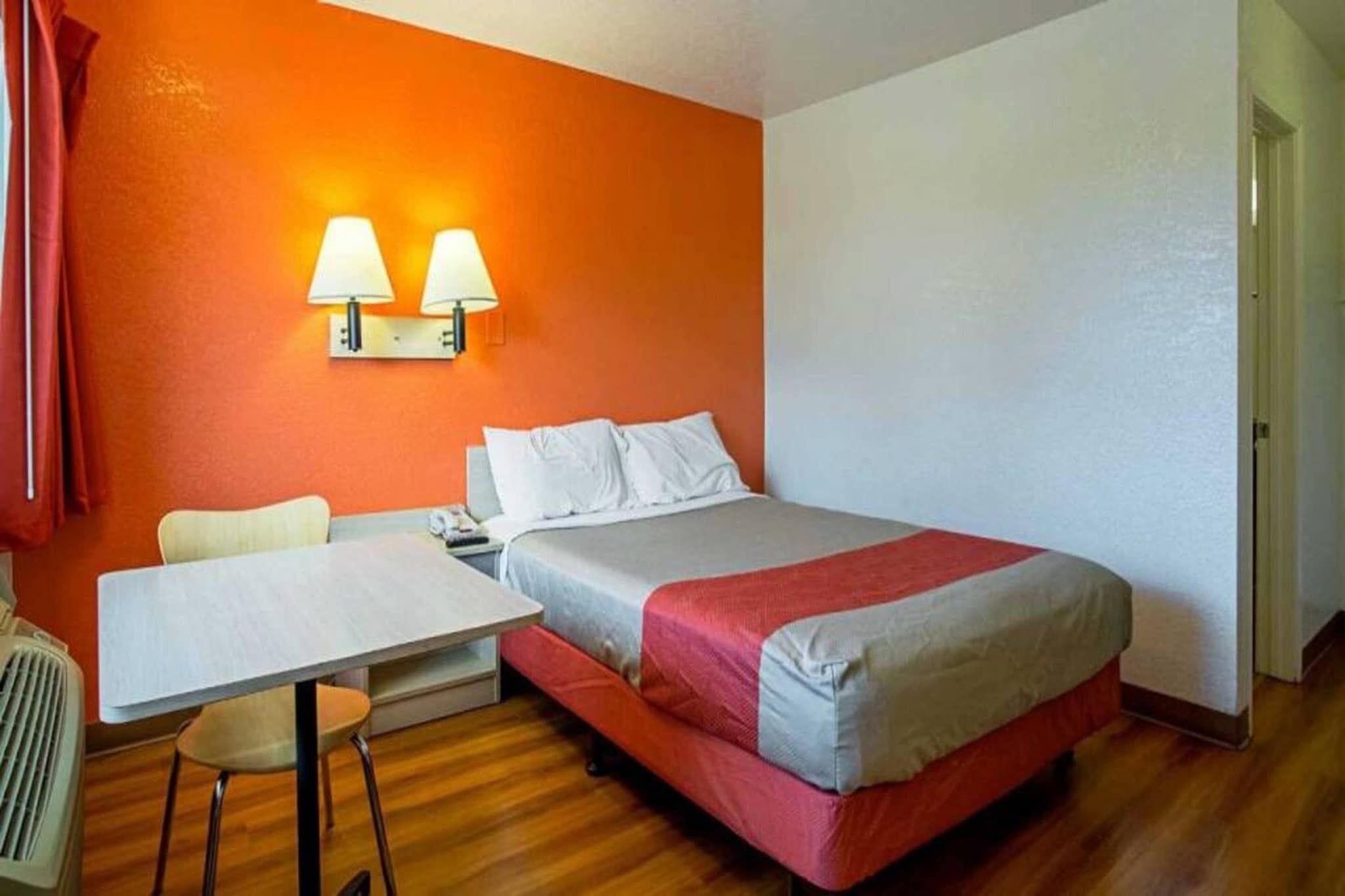 Una habitación de hotel con una cama, un escritorio, una silla y dos lámparas fijadas a la pared.